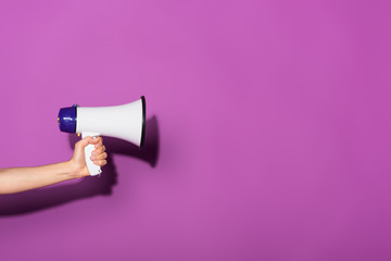 Wall Mural - cropped image of woman holding megaphone on purple background