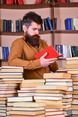 Leinwandbilder - Education and science concept. Teacher or student with beard studying in library between piles of books. Man on busy thoughtful face reading book, bookshelves on background.