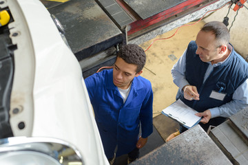 skilled mechanics in coveralls working under a lifted up car