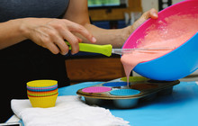 Woman Pouring Batter Mix Into Cupcake Liners For Baking.  Preparing Food In Bright And Cheery Kitchen.