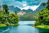 Mountain scenery with with tropical rain forest in the background and blue water lake in the foreground during a sunny day at Ratchaprapha Dam at Khao Sok National Park, Surat Thani Province, Thailand