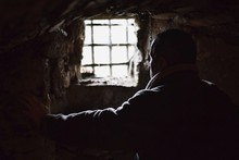 Man Prisoner Watching Out From Underground Window, Hands On The Wall