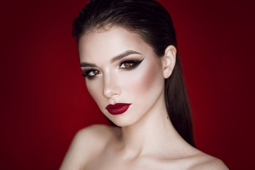 beautiful brunette girl with bright makeup in the studio on a red background