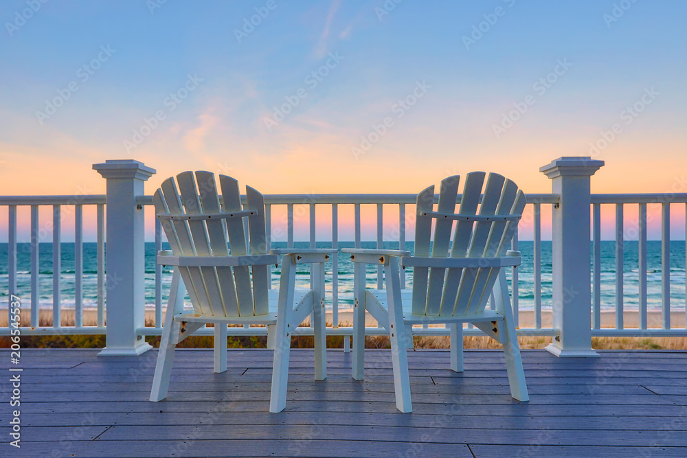 Adirondack Chair sits on the balcony deck of a house looking out over the beach and the ocean - obrazy, fototapety, plakaty 