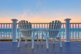 Fototapeta Pomosty - Adirondack Chair sits on the balcony deck of a house looking out over the beach and the ocean