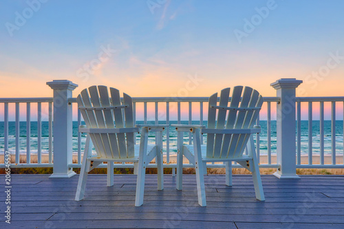Fotomural Adirondack Chair sits on the balcony deck of a house looking out over the beach