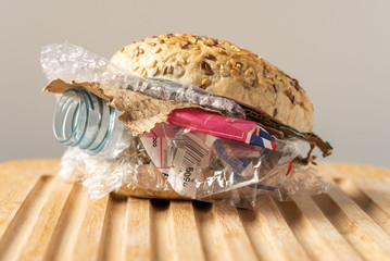 fresh tasty burger with plastic waste and paper cardboard inside on wooden board. recycled waste in 