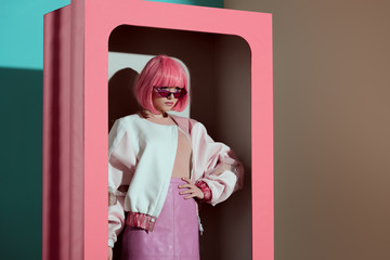 beautiful fashionable girl in pink wig posing with hand on waist in decorative box