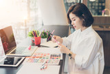 Fototapeta  - Young woman designer choosing colored pencils and color samples sheets for selection on office desk.