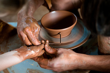 Potter's hands guiding child's hands to help him to work with the pottery wheel