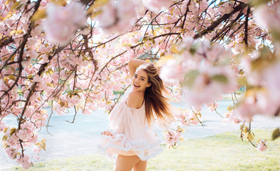 Woman with gorgeous smile having fun in blooming garden. Female with slim sexy body on natural background, wellness and fitness concept. Sensual blond girl in short chiffon dress walking in park