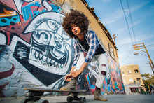 African American Girl Stands On Skateboard With Wall On Background