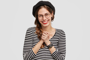 Wall Mural - People, positive emotions concept. Attractive French woman being very pleased, keeps hands together, smiles broadly, hears good words about her country, enjoys communication with foreign people