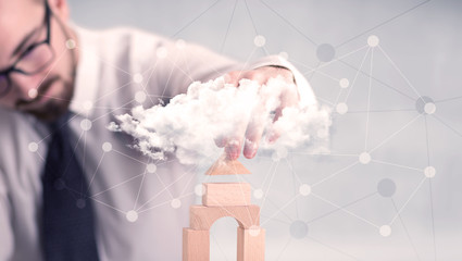 Young handsome businessman using wooden building blocks behind cloud concept 