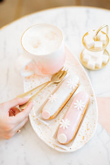 Wall Mural - Delicious handmade eclairs with pink glaze and a Cup of coffee on the table in the cafe. Pink background.