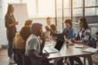 © Yakobchuk Olena - Happy male telling by mobile while situating at desk near beaming colleagues during conference in office. Glad lady standing near board