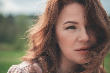 Close up portrait of pensive middle-aged red-haired woman relaxing in the nature 