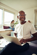 © Flamingo Images - Smiling African businessman using a laptop at his office desk