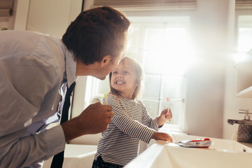 Father teaching daughter how to brush teeth