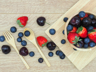 Fresh summer fruits, Cherry, strawberry and blueberry in wooden bowl isolated on wood background.