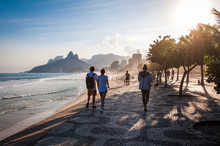 People Walk On The Famous Sidewalk Of Ipanema Beach By Sunset