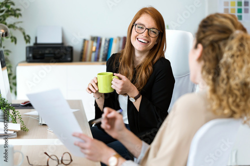 Fotografía Two pretty young business woman relaxing one moment while drinking coffee in the office