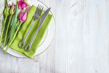 Wall Mural - Festive table setting: tulips on green napkin and white plate on white wooden background with copy space