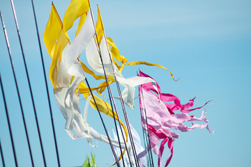 A waving yellow-white and pink-petal long triungular flags on a background bright blu sky