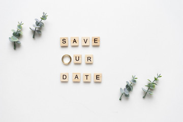 Wooden letters  spelling save our date, oregano branches and wedding rings on white marble. Top view.