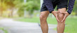 Young fitness man holding his sports leg injury, muscle painful during training. Asian runner having knee ache and problem after running and exercise outside in summer