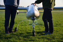 Man preparing unmanned aerial vehicle drone with light and camera for takeoff on ground, green grass airfield, sunny summer morning