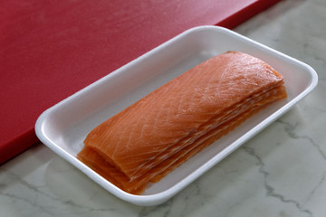 Fillet of red salmon fish in a white rectangular cup next to a cutting board. Ingredient for cooking for sushi and rolls. Japanese food.