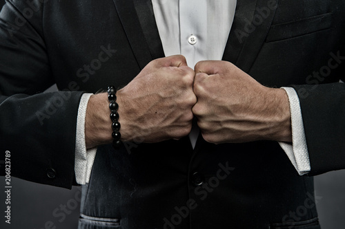 Fotomural Male fists with swollen veins and bracelet on formal suit background