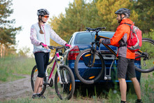 Young Couple Unmounting Mountain Bikes From Bike Rack On The Car. Adventure And Family Travel Concept.
