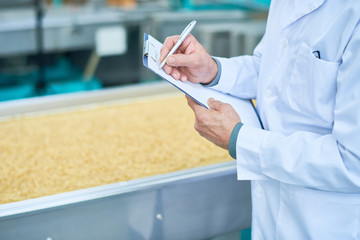 Wall Mural - Close up  of  factory worker doing  production quality inspection in food industry holding clipboard and standing by conveyor belt, copy space