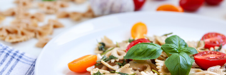 Panoramic view on farfalle aglio olio on a white plate with cherry tomatoes and fresh basil