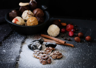 Wall Mural - A variety of truffles in a black clay pile, walnut kernels and prunes under powdered sugar, cinnamon sticks and fresh cranberries