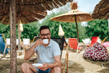 Fototapeta Miasto - Young smiling man enjoying coffee at the beach.