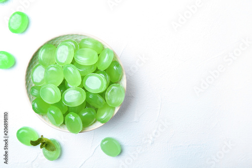 Plakat Bowl with tasty mint candies and leaves on light background, top view