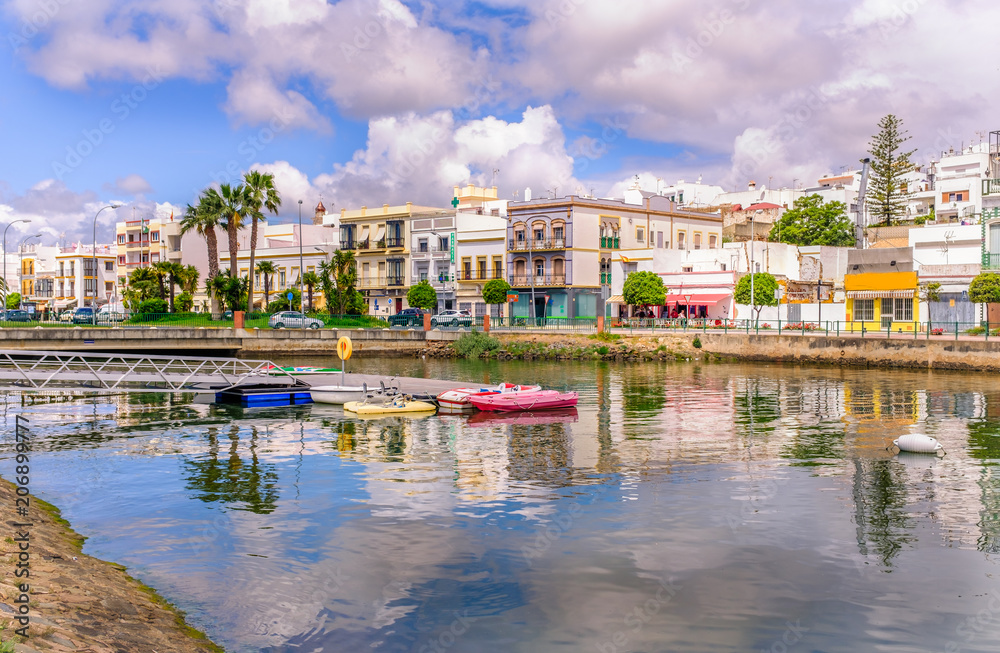 Traditional white architecture of the region along the riverbank in Ayamonte, Huelva province, Andalucia, Spain.  There are pleasure paddle boats on river that runs into the Guadiana River.  Ayamonte  - obrazy, fototapety, plakaty 