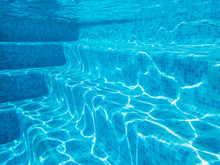 Underwater Image Of Swimming Pool Steps With Sunlight Causing Patterns On The Tiled Blue Steps