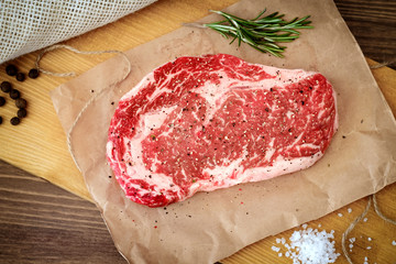 Raw rib eye steak on a wooden Board prepared for the grill. Top view