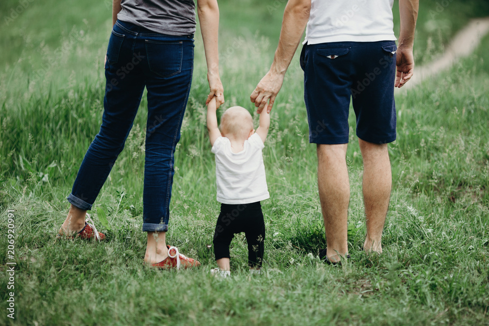 Happy family walking in the park. Mom, dad and daughter walk outdoors, parents holding the baby girl's hands. Childhood, parenthood, family bonds, marriage concept - obrazy, fototapety, plakaty 
