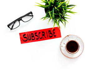 Poster - Email subscribe concept. Hand lettering subcribe on work desk with plant, glasses, cup of coffee on white background top view copy space