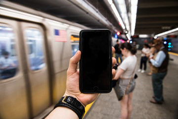 Man using cell phone holding in hand and showing touch screen on subway station in New York City. Empty cell phone screen in urban city setting.