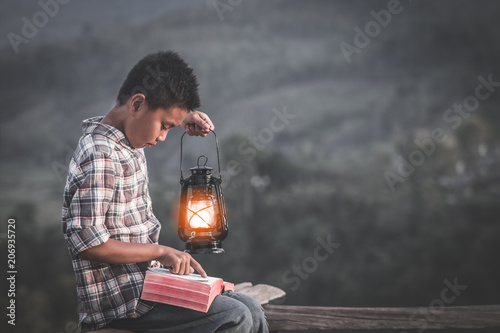 Fotografía Boy holding oil lamp and reading bible, christian concept