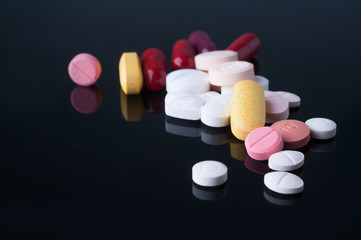 Wall Mural - Medical pills with different size, shape and color on black glass table with reflection.Studio shot.