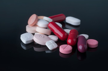 Wall Mural - Medical pills with different size, shape and color on black glass table with reflection.Studio shot.