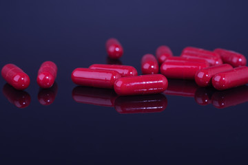 Wall Mural - Red medical capsules or pills on black table with reflection.Studio shot.