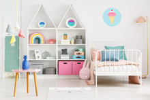 Front View Of A Kid's Room With A Table, Shelves With Boxes And Rainbow, Single Bed And Ice Cream Poster On The Wall